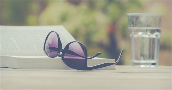 A pair of sunglasses rest on a book next to a glass of water.