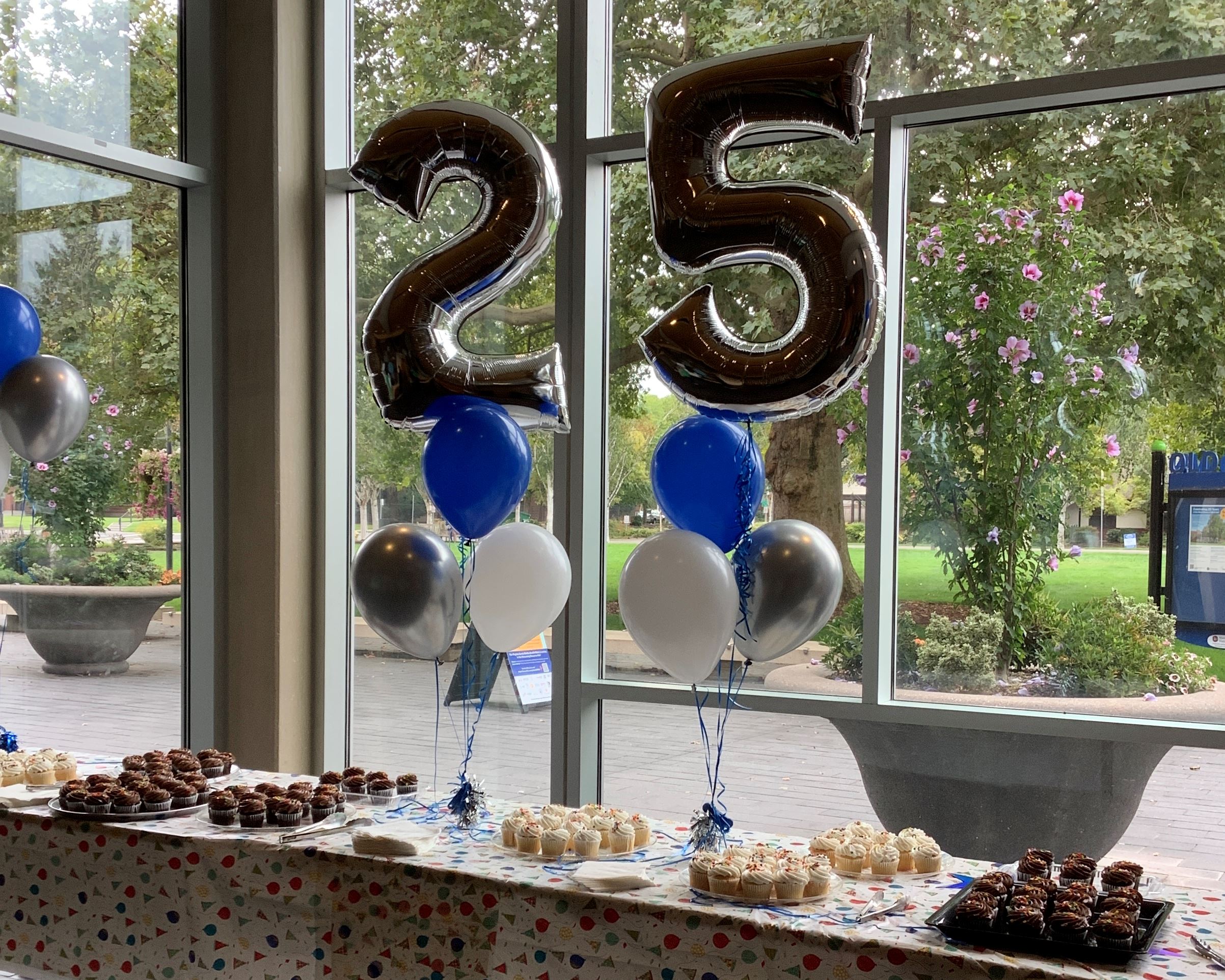 Balloons in the shape of a 2 and a 5 and other balloons with cupcakes on a table.