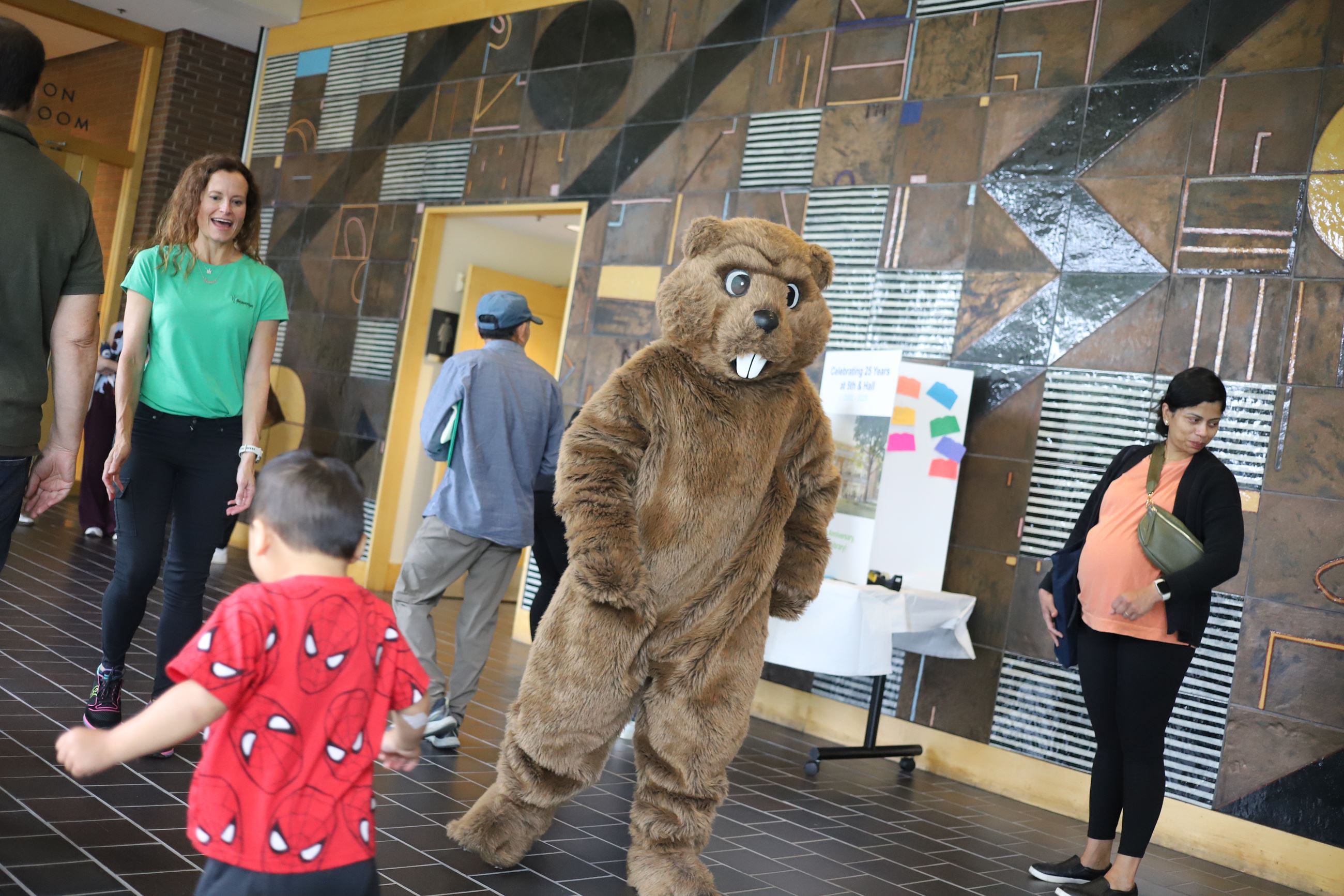 A person in a beaver costume dancing in a library building with other people dancing.