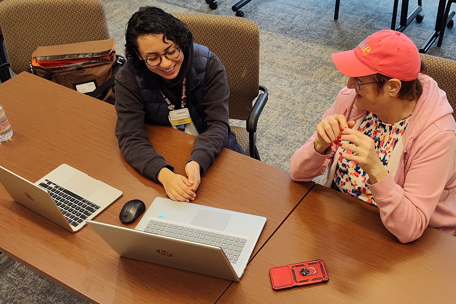 Two people sitting a table with laptops, smiling.