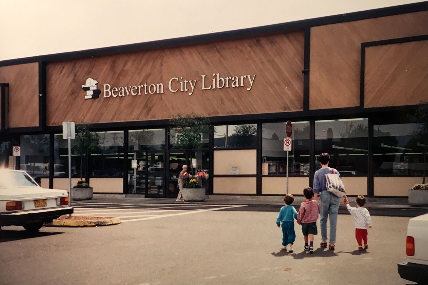 Photo from the early 1980s of the exterior of a library building with a family walking up.