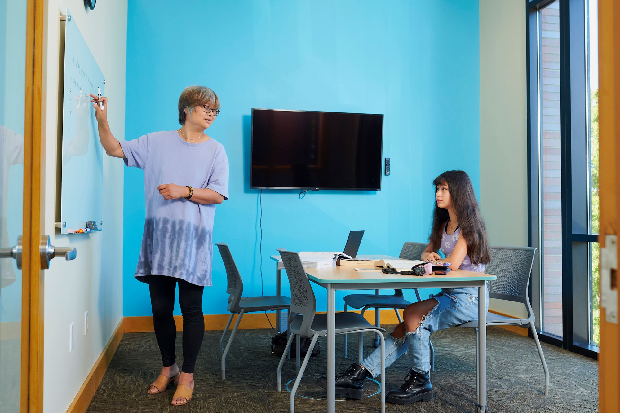 Photo of two people using a study space with a table, monitor, and dry-erase board.
