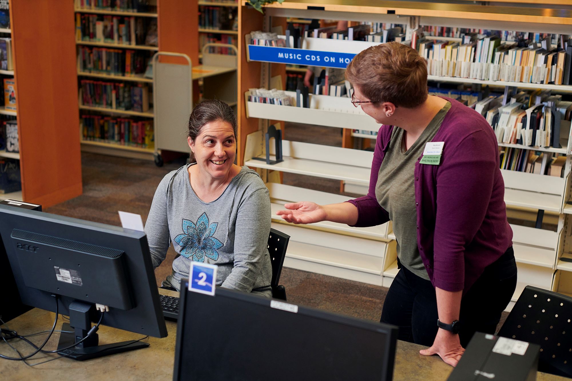 Photo of two people at a computer in a public library building.