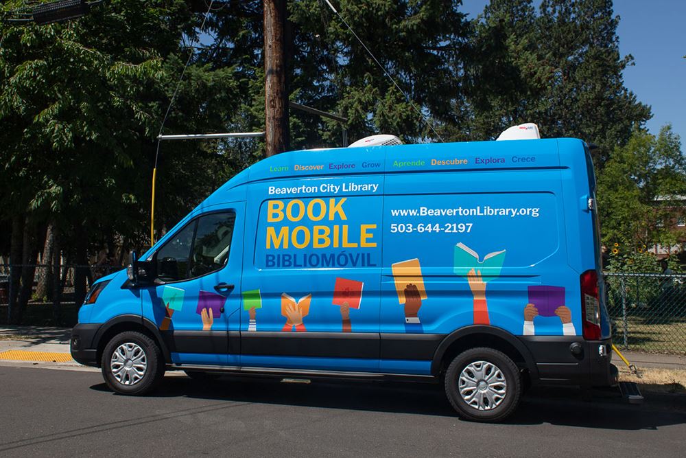 Photo of a blue bookmobile van with illustrations of hands holding up books along the bottom.