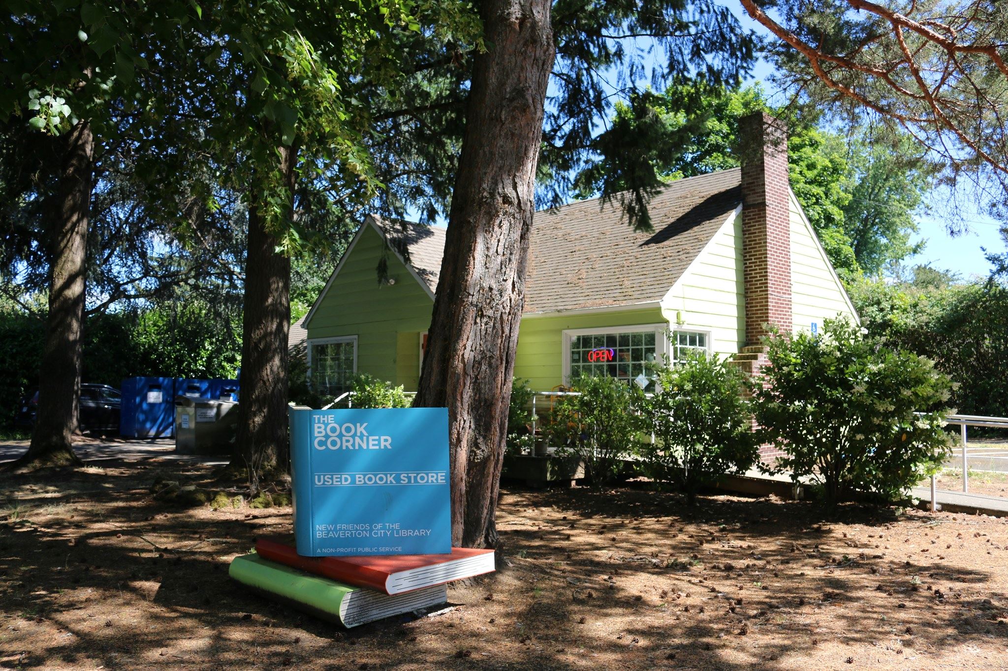 Photo of a green house with a large sign made out of blue, red, and green books outside of it.