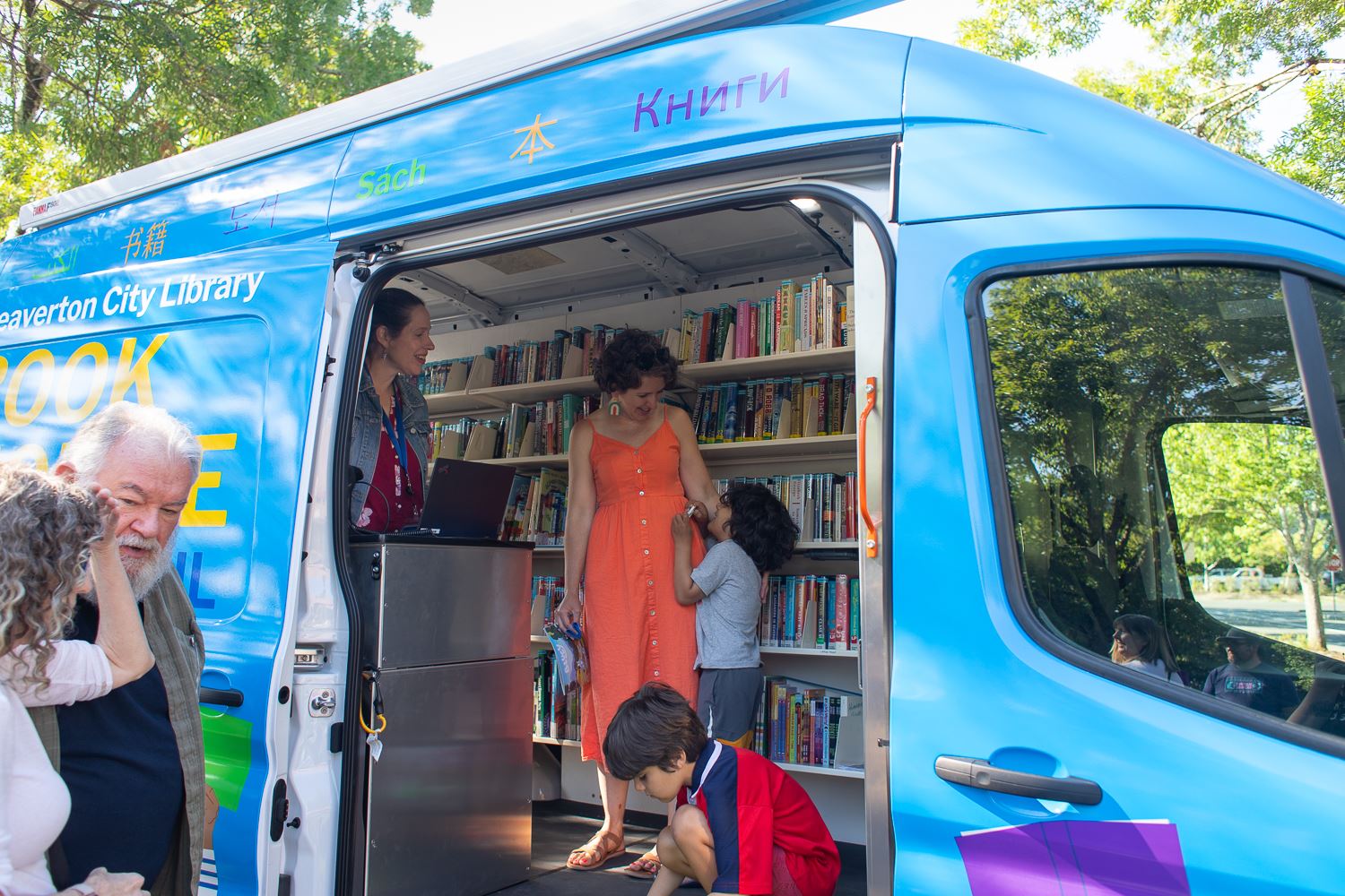 Photo of the inside of a bookmobile van with shelves of books lining one wall and people inside.