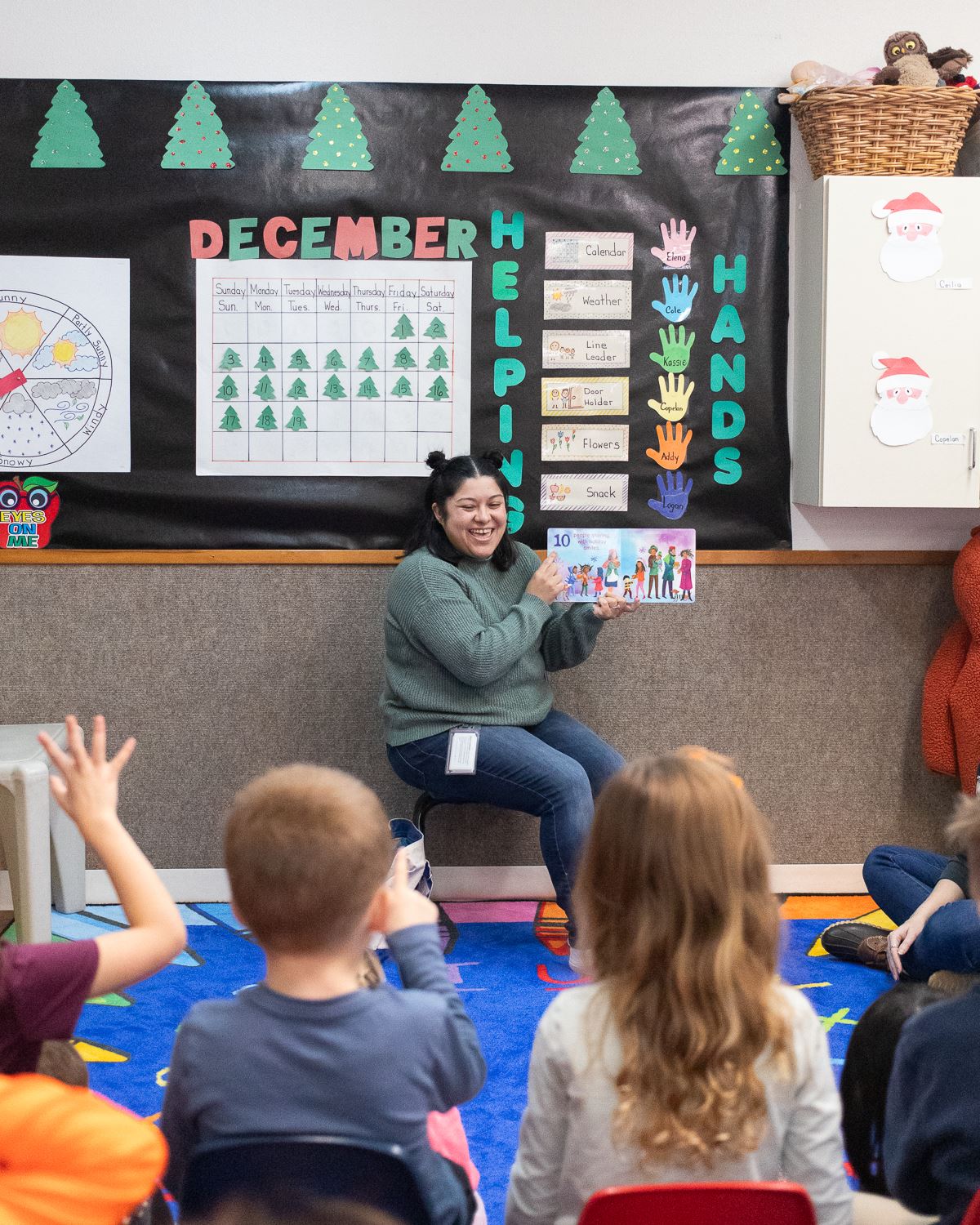 Photo of a woman at the front of a class of young students holding open a book and smiling.