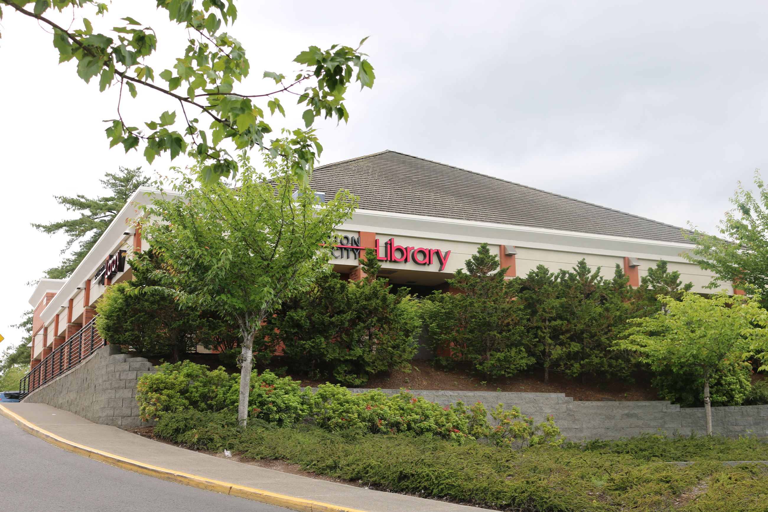Photo of a library building with trees and greenery and an overcast sky.